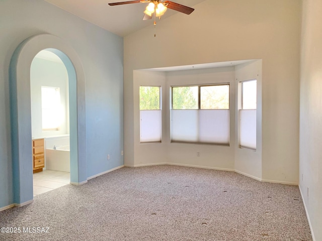 unfurnished room with arched walkways, a ceiling fan, carpet flooring, vaulted ceiling, and baseboards