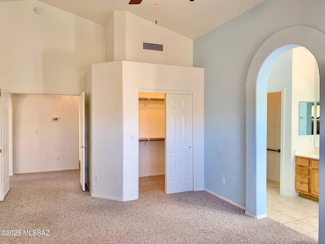 unfurnished bedroom with visible vents, arched walkways, light colored carpet, high vaulted ceiling, and a closet