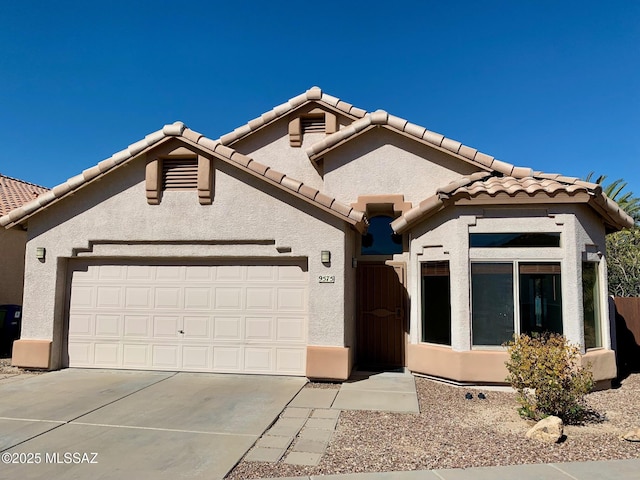 view of front of house with an attached garage, driveway, a tiled roof, and stucco siding