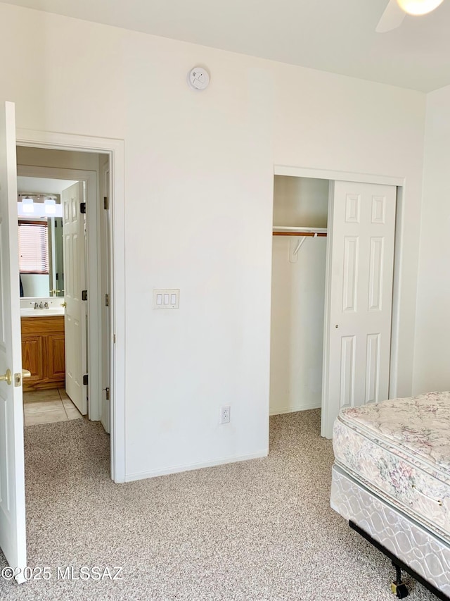 unfurnished bedroom featuring light carpet, a sink, a ceiling fan, and a closet