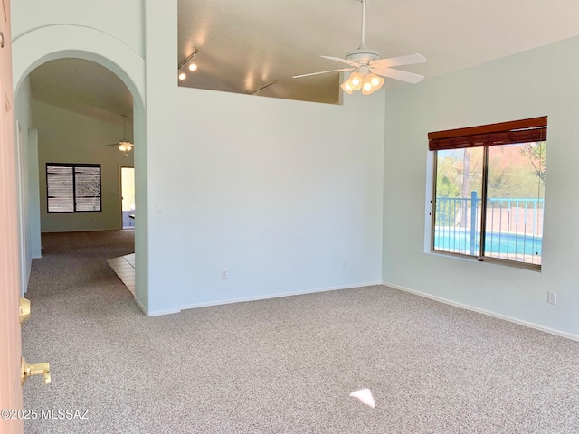 empty room with arched walkways, a ceiling fan, lofted ceiling, rail lighting, and carpet flooring