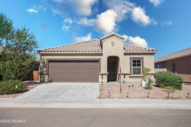 mediterranean / spanish house with a garage, concrete driveway, a tile roof, and stucco siding