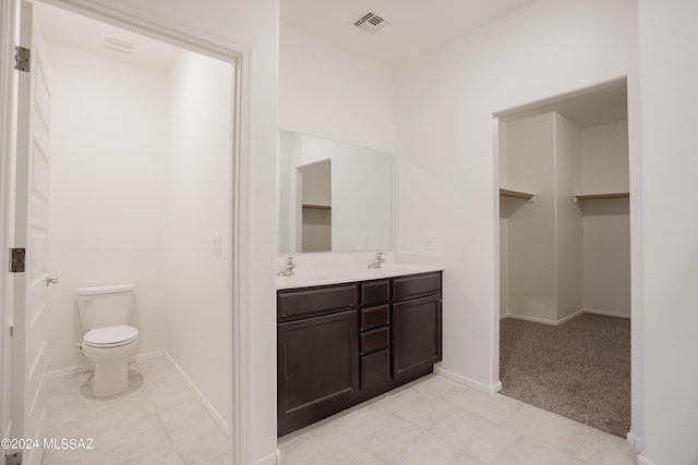 bathroom with double vanity, visible vents, toilet, a sink, and baseboards