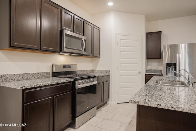 kitchen with light tile patterned floors, a sink, dark brown cabinets, appliances with stainless steel finishes, and light stone countertops