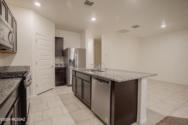 kitchen featuring visible vents, appliances with stainless steel finishes, a kitchen island with sink, a sink, and light stone countertops