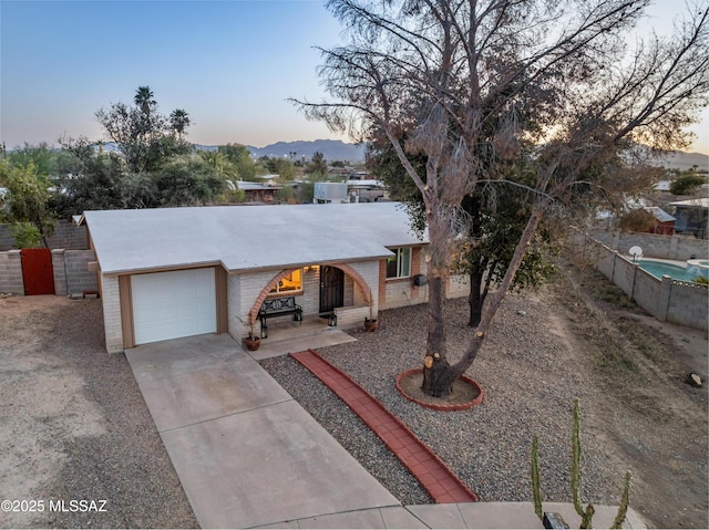 ranch-style house featuring brick siding, fence, driveway, a garage, and a mountain view