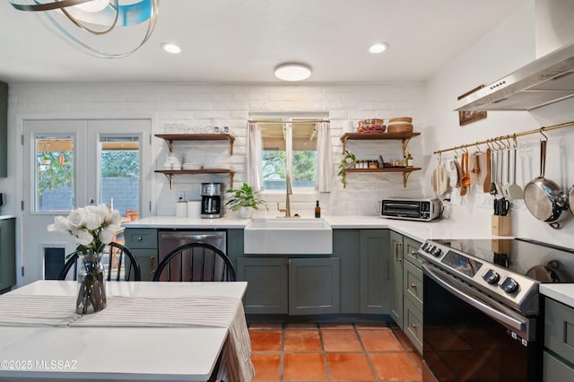 kitchen with dishwashing machine, open shelves, a sink, electric stove, and wall chimney exhaust hood