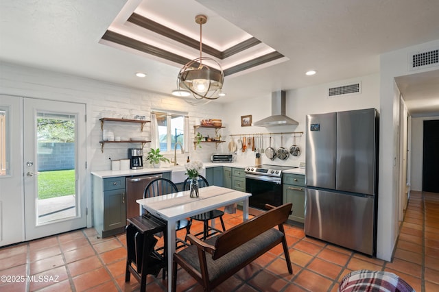 kitchen with a tray ceiling, wall chimney exhaust hood, visible vents, and stainless steel appliances