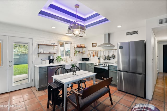 kitchen featuring visible vents, a tray ceiling, open shelves, stainless steel appliances, and wall chimney range hood