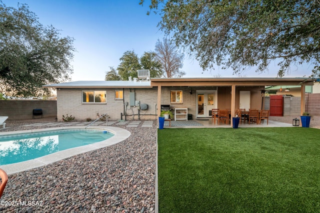 rear view of property featuring brick siding, a lawn, a patio, and fence