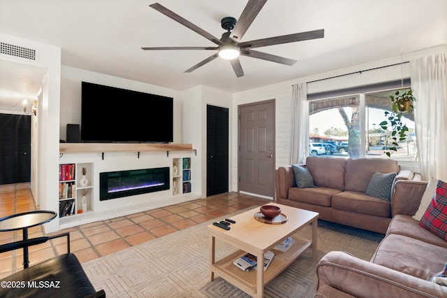 living room with tile patterned floors, visible vents, a ceiling fan, and a glass covered fireplace