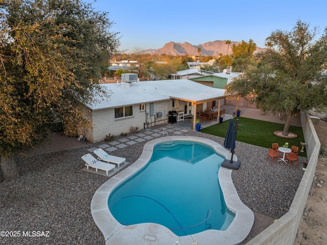 pool with outdoor dining space, a patio, a fenced backyard, a mountain view, and a yard