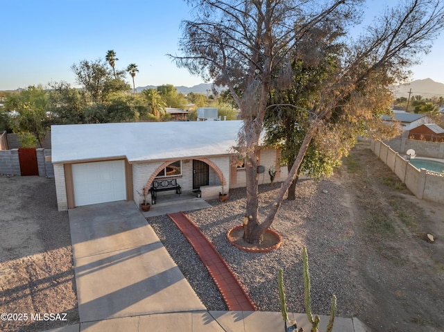 ranch-style house featuring a mountain view, concrete driveway, an attached garage, and fence