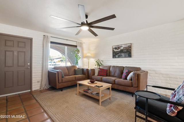 tiled living room featuring a ceiling fan and brick wall