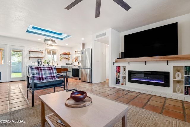 living area featuring visible vents, recessed lighting, a skylight, a glass covered fireplace, and a raised ceiling