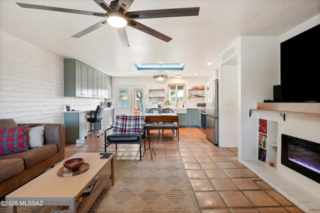 living room featuring a glass covered fireplace, visible vents, brick wall, and light tile patterned flooring