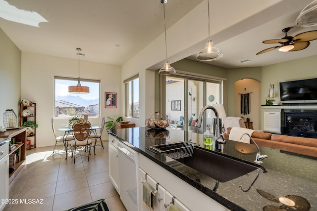 kitchen with light tile patterned floors, arched walkways, white cabinets, white dishwasher, and a sink