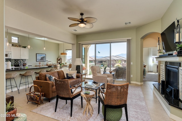 living area featuring light tile patterned floors, visible vents, arched walkways, and a glass covered fireplace