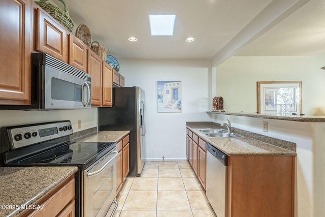 kitchen with stone countertops, a peninsula, a sink, appliances with stainless steel finishes, and brown cabinetry