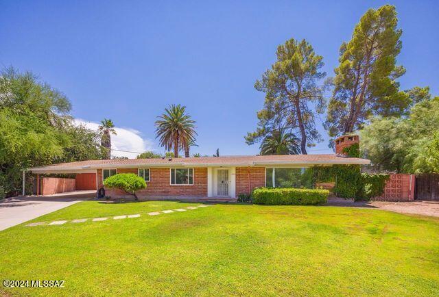 single story home featuring brick siding, concrete driveway, fence, a carport, and a front lawn