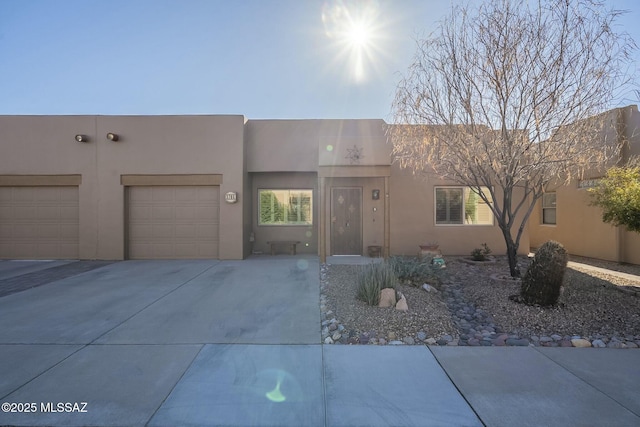 pueblo-style house with driveway, an attached garage, and stucco siding