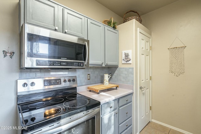 kitchen with light tile patterned floors, stainless steel appliances, light countertops, gray cabinetry, and backsplash