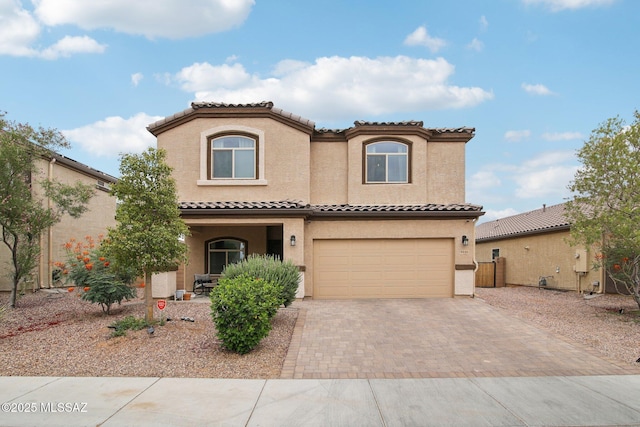 mediterranean / spanish-style house with a garage, decorative driveway, a tiled roof, and stucco siding