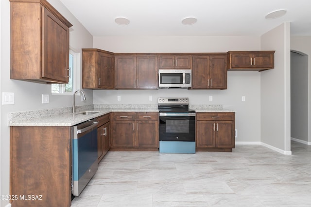 kitchen featuring a sink, light stone counters, stainless steel appliances, arched walkways, and baseboards