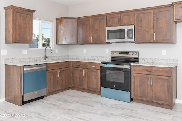 kitchen with a sink, light stone countertops, and stainless steel appliances