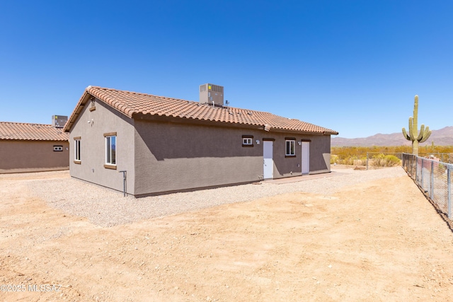 back of property with central AC unit, a mountain view, a tiled roof, fence, and stucco siding