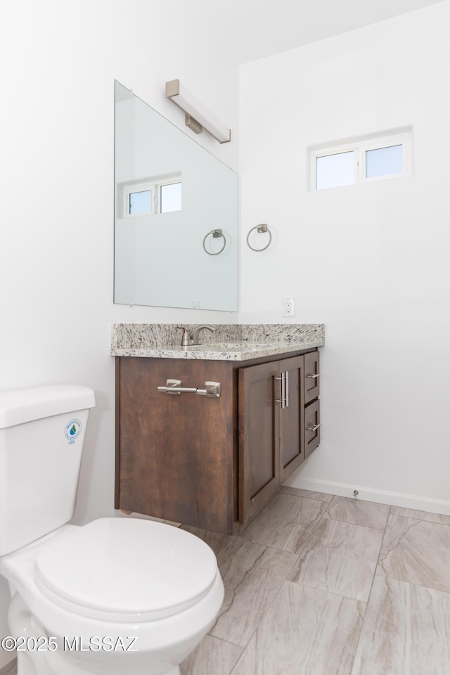 half bath with toilet, vanity, marble finish floor, and baseboards