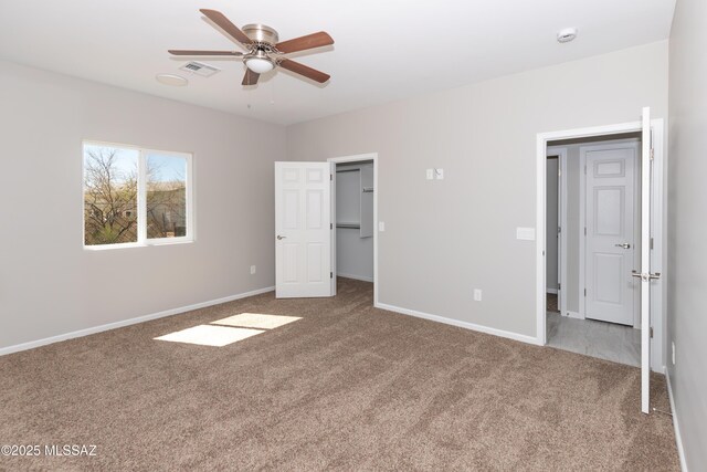 unfurnished bedroom featuring carpet, a ceiling fan, a spacious closet, visible vents, and baseboards