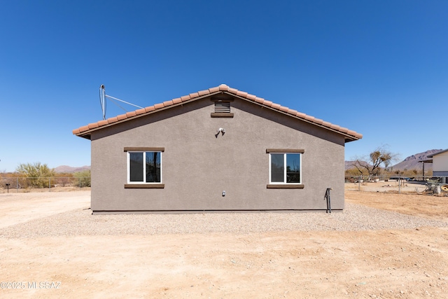 rear view of property featuring stucco siding, a tiled roof, and fence