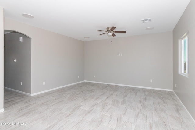 spare room with arched walkways, visible vents, a ceiling fan, and baseboards