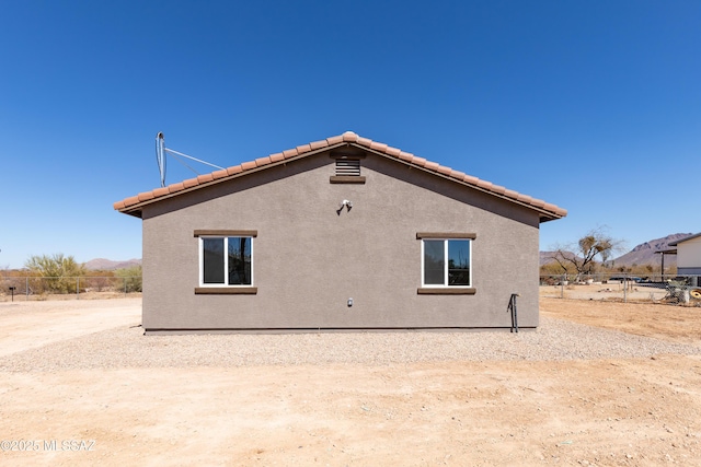 rear view of property featuring stucco siding, fence, and a tile roof