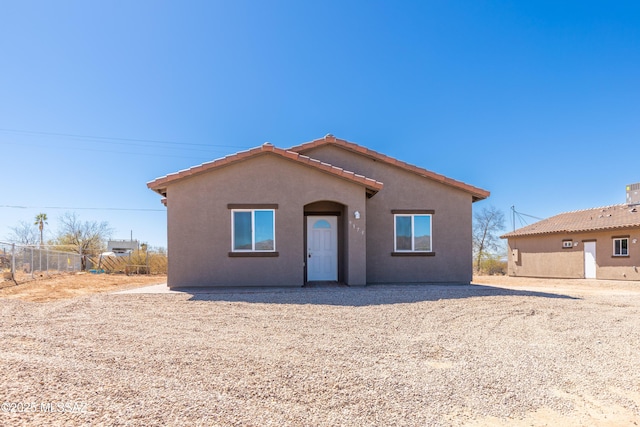 view of front facade featuring a tiled roof, stucco siding, and fence