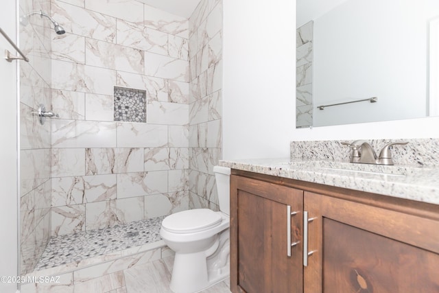bathroom with a tile shower, vanity, and toilet