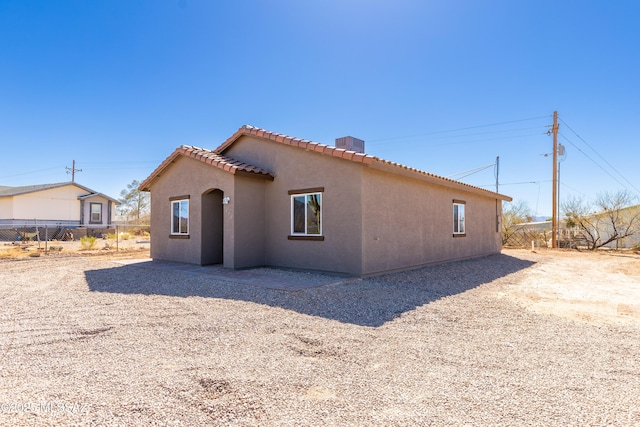 rear view of property featuring a tiled roof, stucco siding, fence, and a chimney