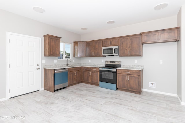 kitchen with a sink, baseboards, light stone counters, and stainless steel appliances