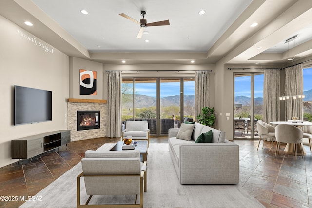 living room with stone tile floors, a stone fireplace, recessed lighting, a mountain view, and a raised ceiling