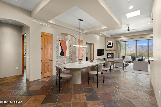 dining area with a ceiling fan, recessed lighting, a fireplace, stone tile flooring, and a raised ceiling