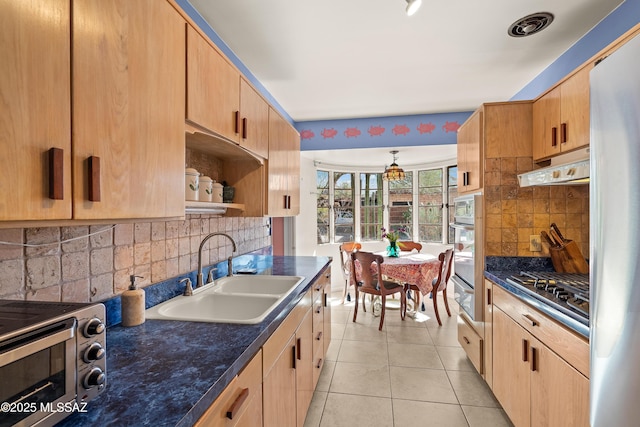 kitchen featuring a sink, dark countertops, under cabinet range hood, and stainless steel gas stovetop