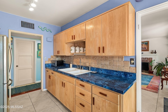 kitchen with visible vents, a sink, backsplash, freestanding refrigerator, and light tile patterned floors