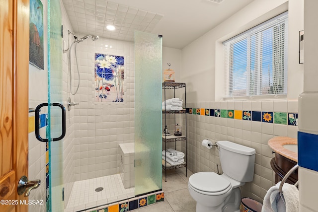 full bath featuring a wainscoted wall, toilet, a stall shower, tile patterned floors, and tile walls