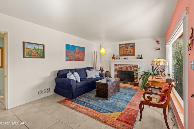 living area with tile patterned floors, visible vents, and a brick fireplace