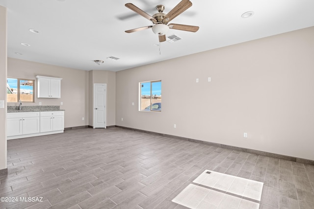 unfurnished living room with ceiling fan, a sink, visible vents, baseboards, and light wood-type flooring