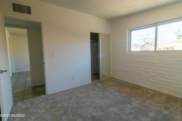 unfurnished bedroom with tile patterned flooring, visible vents, carpet flooring, a closet, and a textured ceiling