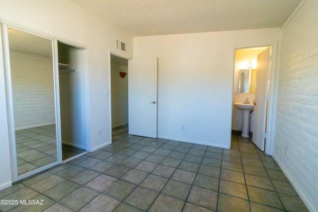 unfurnished bedroom with visible vents, tile patterned floors, a closet, a textured ceiling, and a sink