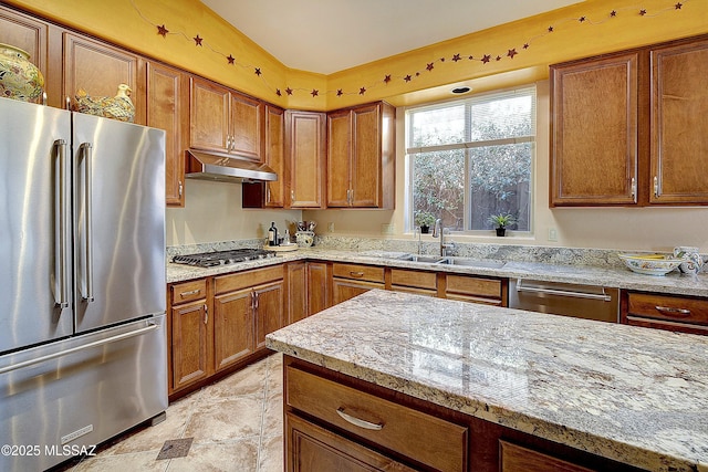 kitchen featuring light stone counters, brown cabinets, stainless steel appliances, under cabinet range hood, and a sink