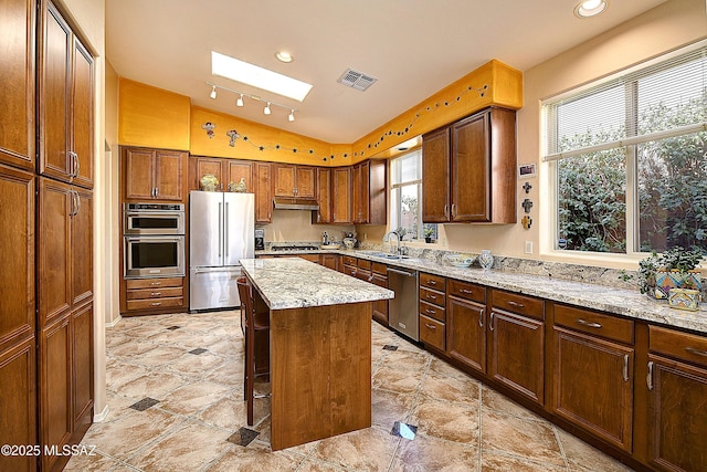 kitchen with visible vents, appliances with stainless steel finishes, light stone counters, a center island, and a sink